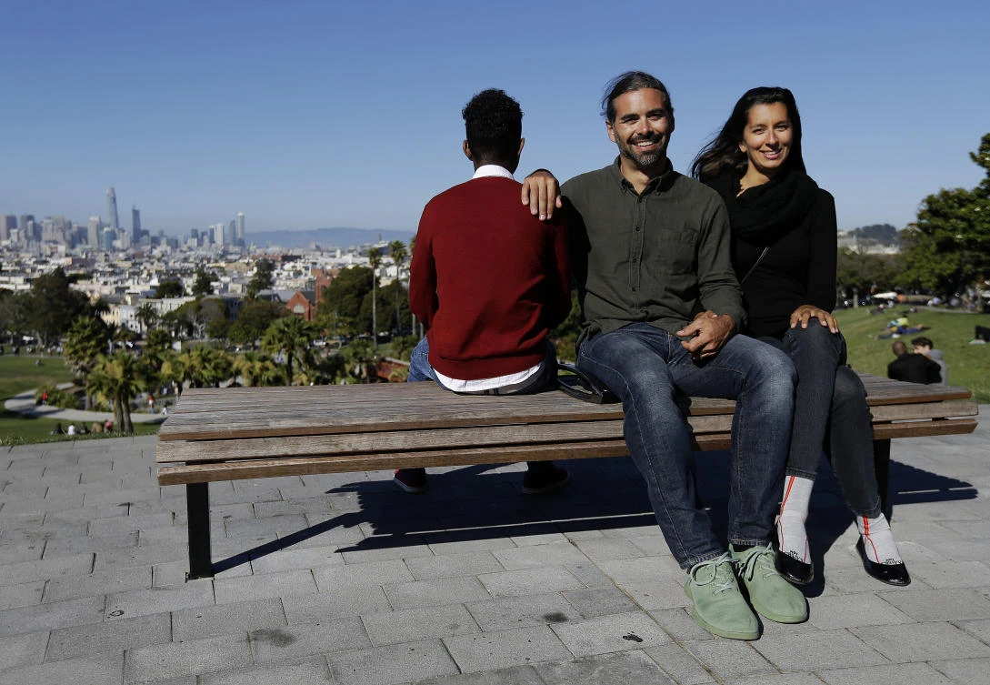 In this July 14, 2017 photo, Mike Gougherty, center, and Julie Rajagopal, right, pose for photos with their 16-year-old foster child from Eritrea at Dolores Park in San Francisco. When their 16-year-old foster child landed in March, he was among the last refugee foster children to make it into the U.S. Trump administration travel bans declared to block terrorists also are halting a small, three-decade-old program bringing orphan refugee children to waiting foster families in the United States. (AP Photo/Jeff Chiu)