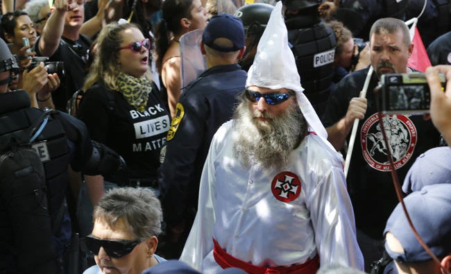 This July 8, 2017 photo shows members of the KKK escorted by police past a large group of protesters during a KKK rally in Charlottesville, Virginia. GoDaddy and Google on Monday revoked the Neo-Nazi website the Daily Stormer, saying the site had violated their terms of service. (AP Photo/Steve Helber)