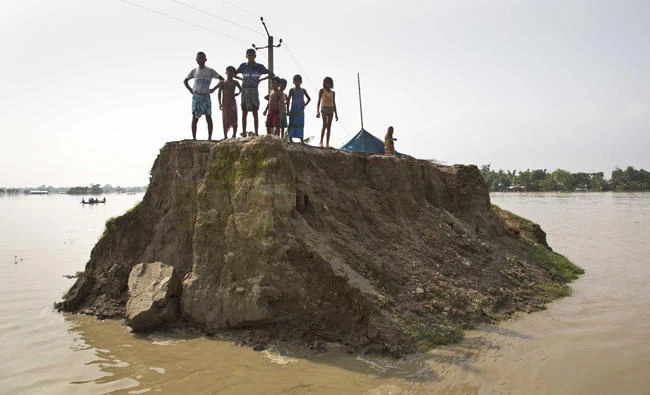 Flood-affected villagers wait for relief material on a broken road washed away by floodwaters in Morigaon district, east of Gauhati, northeastern state of Assam, on Tuesday. (AP Photo/Anupam Nath)