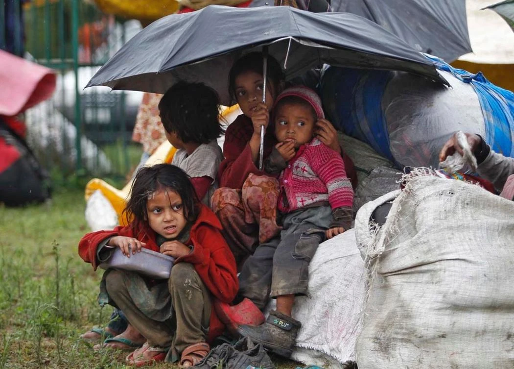 Kashmiri children with their belongings sit under an umbrella during rain in Srinagar. (Reuters)