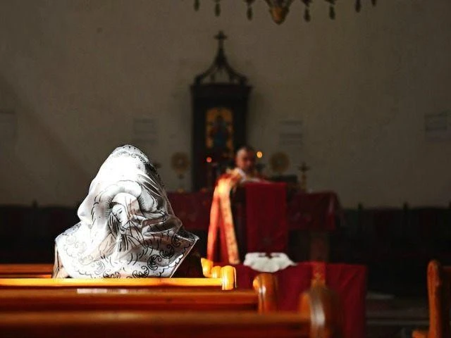 Syrian woman is sitting in church and priest is seen in the background. (File photo by AFP)