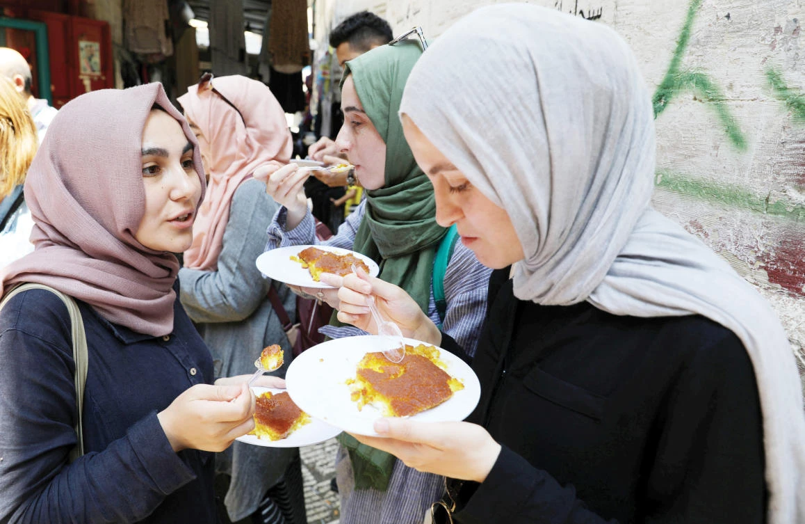Tourists eat knafa, a sweet semolina and cheese pastry, outside Al-Aqsa sweet shop in the historic covered market of Nablus in the West Bank. (Reuters)
