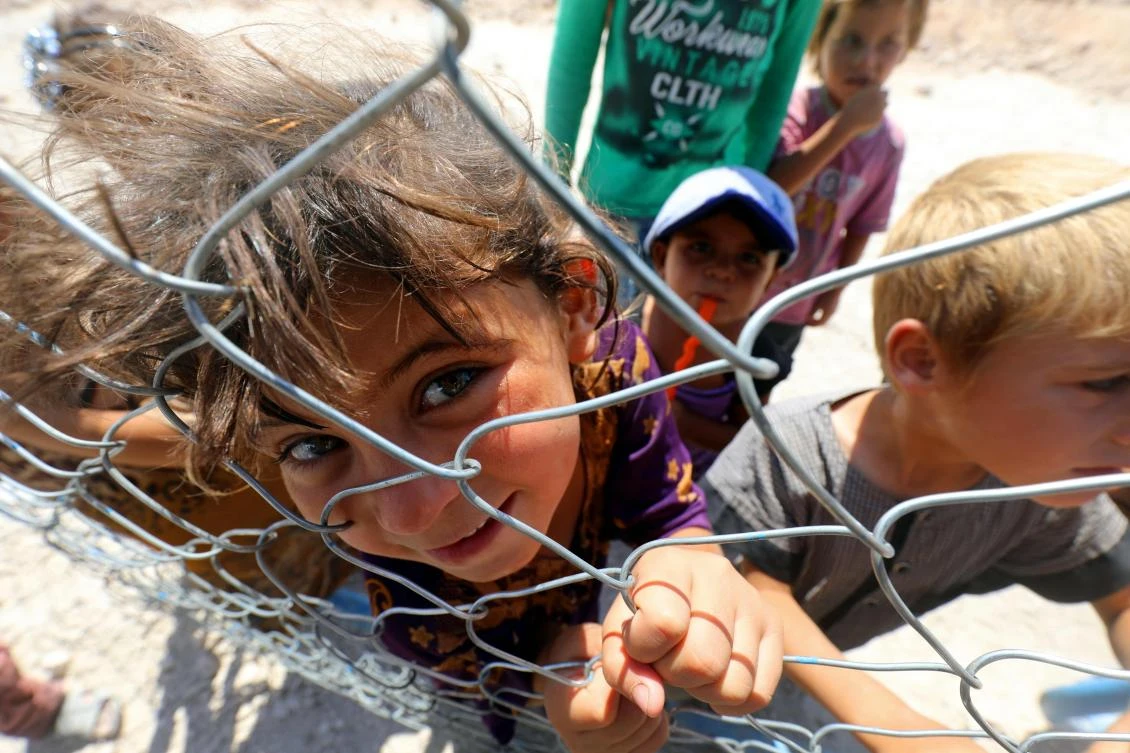 Displaced children from the Islamic State (IS) group's Syrian stronghold of Raqa, pose for a photo behind a fence at a camp in Ain Issa on August 22, 2017. (AFP)