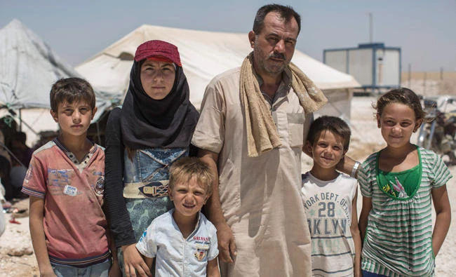 A photo released by Save The Children shows a resident from Raqqa standing with his children outside a tent in Ain Issa, Syria. (AFP)