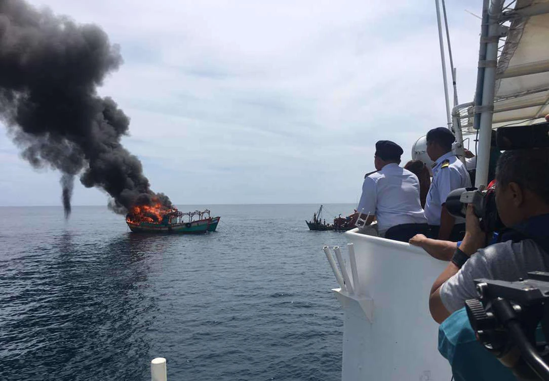 In this handout photo, Maritime Enforcement Ageny personnel, right, watch the burning of a foreign fishing boat at Tok Bali in Kelantan, Malaysia, on August 30, 2017. (Malaysia Maritime Enforcement Agency via AP)