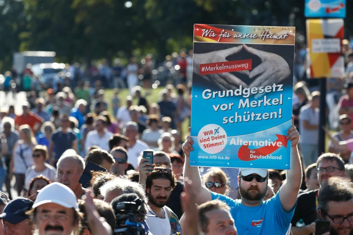 A supporter of the right-wing populist Alternative for Germany (AfD) holds up a placard which reads "Protect the constitution from Merkel" as German Chancellor Angela Merkel addresses an election campaign rally of the Christian Democratic Union (CDU) in Bitterfeld, eastern Germany on August 29, 2017, less than a month before the September 24th general election. (AFP)