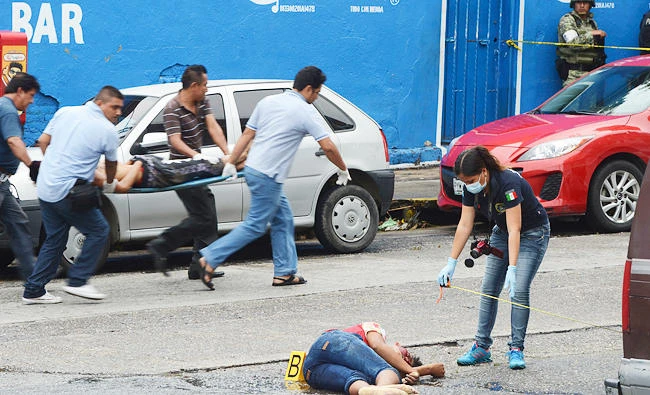 A police officer inspects a body as another body is carried away after they were shot in central Acapulco, Mexico, on Tuesday. (AP)