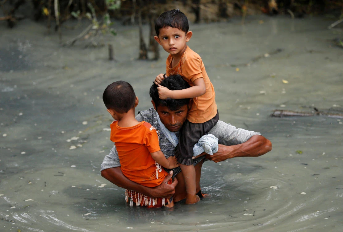 A Rohingya refugee man carries his children as he walks through water after crossing border by boat through the Naf River in Teknaf, Bangladesh, September 7, 2017. REUTERS/Mohammad Ponir Hossain