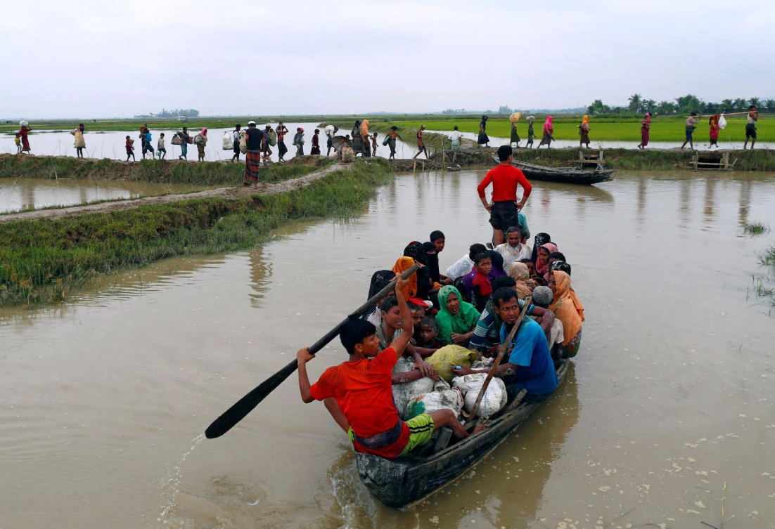 Rohingya refugees travel on a boat as others walk on a muddy path after crossing the Bangladesh-Myanmar border, in Teknaf, Bangladesh, September 6, 2017. REUTERS/Danish Siddiqui