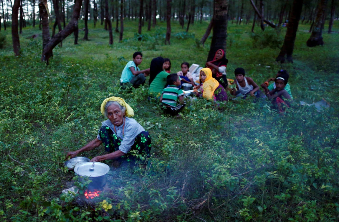 A Rohingya refugee cooks food as others eat after crossing the Bangladesh-Myanmar border by boat through the Bay of Bengal in Teknaf, Bangladesh September 7, 2017. REUTERS/Danish Siddiqui