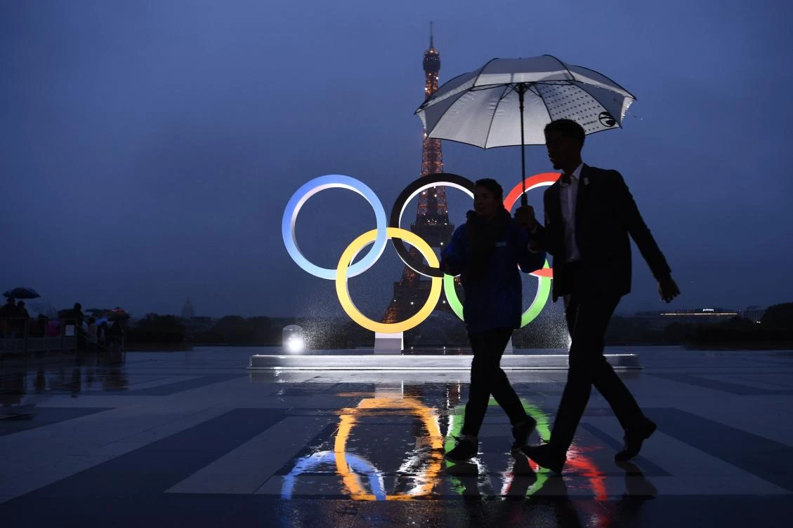 People carrying and umbrella walk past the Olympics Rings on the Trocadero Esplanade near the Eiffel Tower in Paris, on September 13, 2017, after the International Olympic Committee named Paris host city of the 2024 Summer Olympic Games. The International Olympic Committee named Paris and Los Angeles as hosts for the 2024 and 2028 Olympics on September 13, 2017, crowning two cities at the same time in a historic first for the embattled sports body. / AFP / CHRISTOPHE SIMON