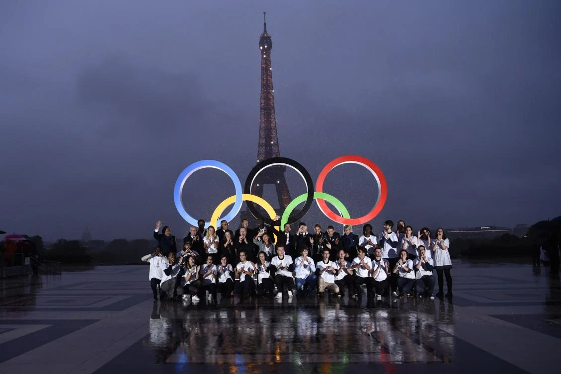 Volunteers pose in front of the Olympics Rings on the Trocadero Esplanade near the Eiffel Tower in Paris, on September 13, 2017, after the International Olympic Committee named Paris host city of the 2024 Summer Olympic Games. The International Olympic Committee named Paris and Los Angeles as hosts for the 2024 and 2028 Olympics on September 13, 2017, crowning two cities at the same time in a historic first for the embattled sports body. / AFP / CHRISTOPHE SIMON