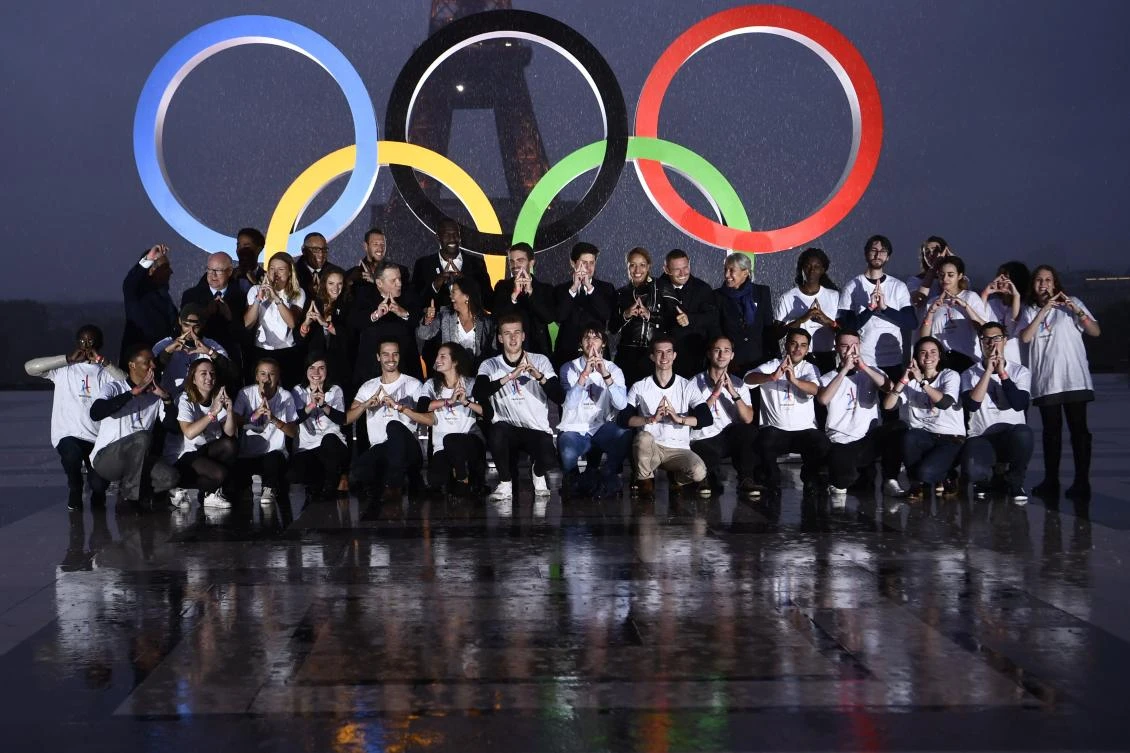 Volunteers pose in front of the Olympics Rings on the Trocadero Esplanade near the Eiffel Tower in Paris, on September 13, 2017, after the International Olympic Committee named Paris host city of the 2024 Summer Olympic Games. The International Olympic Committee named Paris and Los Angeles as hosts for the 2024 and 2028 Olympics on September 13, 2017, crowning two cities at the same time in a historic first for the embattled sports body. / AFP / CHRISTOPHE SIMON