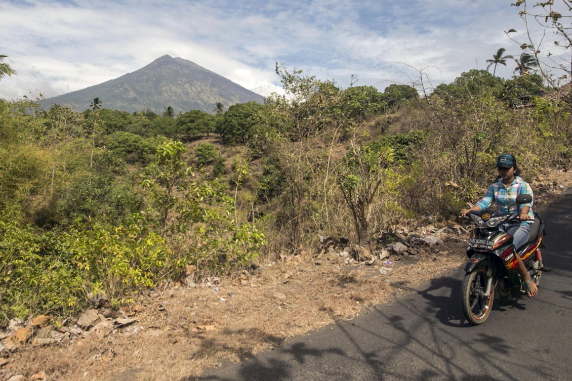A villager rides past by with Mount Agung seen in the background in Karangasem, Bali, Indonesia, on Sunday, September 24, 2017. (File photo by AP)