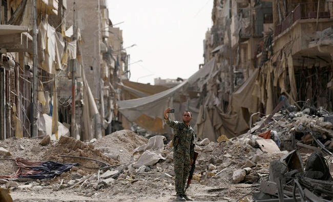 A fighter from Syrian Democratic Forces takes a selfie near a damaged site in Raqqa on Monday. (Reuters)