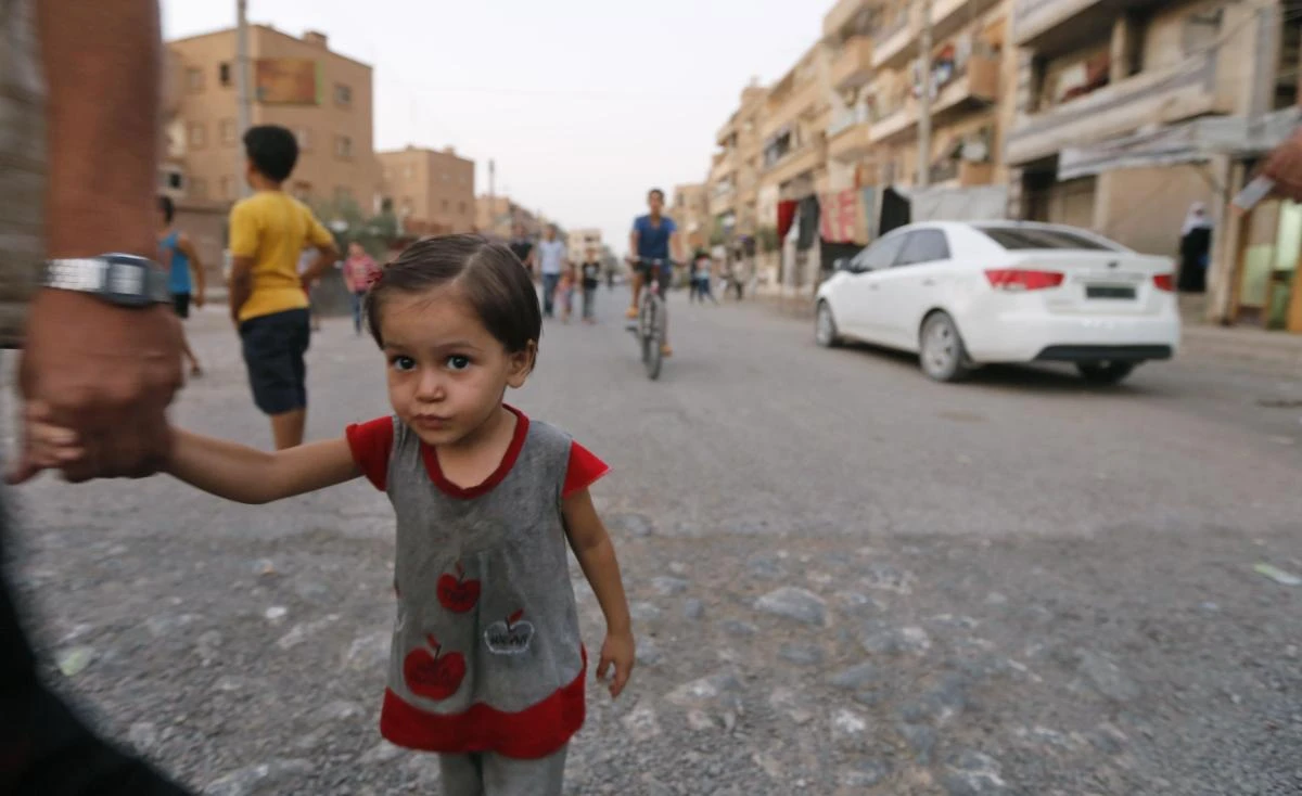 A Syrian man holds the hand of a child as civilians are seen on a street in the eastern city of Deir Ezzor on September 20, 2017 while Syrian government forces continue to press forward with Russian air cover in the offensive against Islamic State group jihadists across the province. Two separate offensives are under way against the jihadists in the area -- one by the US-backed Syrian Democratic Forces, the other by Russian-backed government forces. The Syrian army now controls around 70 percent of the city and is battling to oust IS from the remainder, according to the Britain-based Observatory. (AFP)