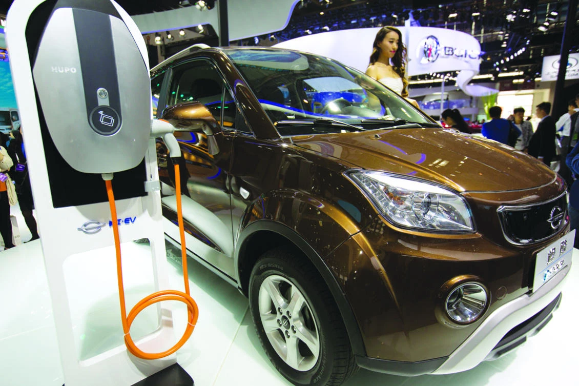 In this April 26, 2016, file photo, a staff member stands next to an e.Cool electric SUV by Chinese automaker Changjiang on display at the Beijing International Automotive Exhibition in Beijing. China has stepped up pressure on automakers to accelerate development of electric cars by raising the first-year target for a planned system of production quotas but delayed its rollout until 2019. (AP Photo/Mark Schiefelbein, File)