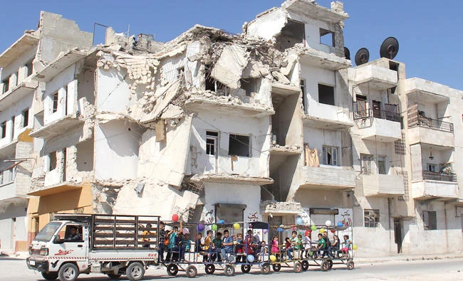 Syrian children ride in decorated carriages along a damaged street in Idlib on Friday, the first day of Eid Al-Adha. (AFP)