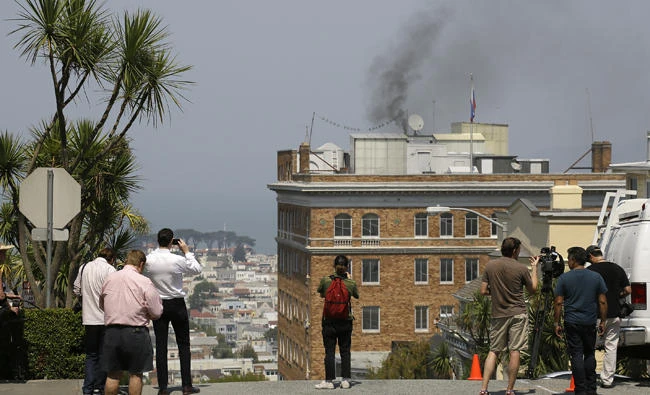 People stop to watch black smoke coming from the roof of the Consulate General of Russia on Sept. 1, 2017, in San Francisco, California. The San Francisco Fire Department says acrid, black smoke seen pouring from a chimney at the Russian consulate in San Francisco was apparently from a fire burning in a fireplace. (AP Photo/Eric Risberg)
