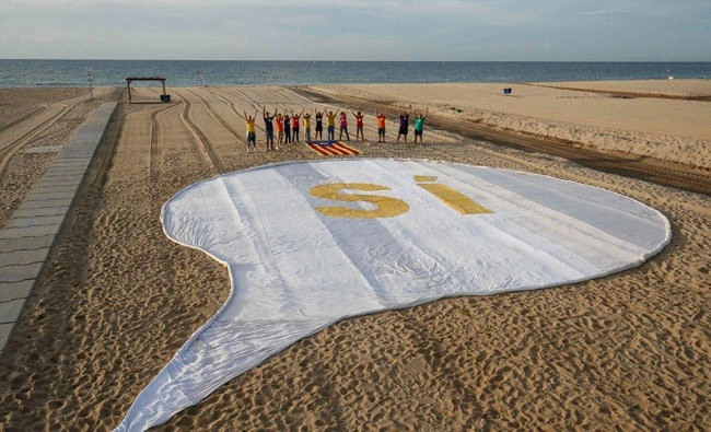 A group of people pose close to a banner reading "SI" (Yes) and "Estelada" flags (Pro-independence Catalan flags) placed on the sand of El Masnou beach near Barcelona, on September 3, 2017, during an action called by ANC (Catalan National Assembly) to support a referendum on independence in Catalonia. (AFP)