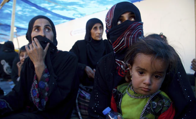 Displaced Iraqi women and children sit on the ground at a collection point west of Mosul on the outskirts of Tal Afar, Iraq on Aug. 26, 2017. (AP Photo/Balint Szlanko, File)