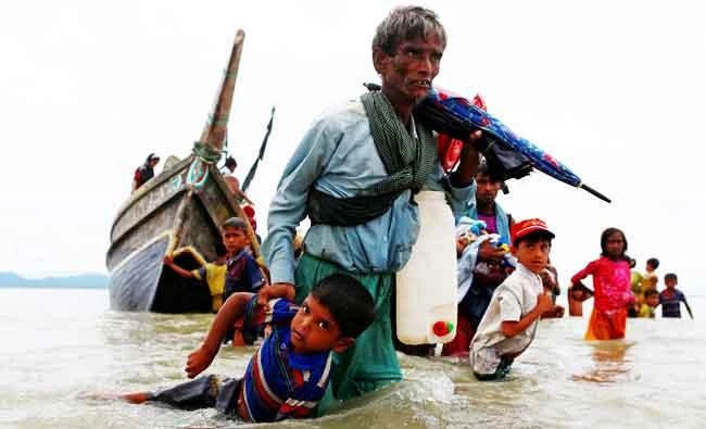 A Rohingya refugee man pulls a child as they walk to the shore after crossing the Bangladesh-Myanmar border by boat through the Bay of Bengal in Shah Porir Dwip, Bangladesh, on Sunday. (REUTERS)