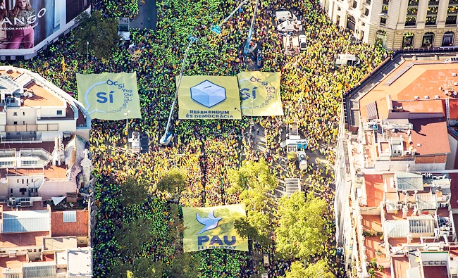 This handout picture released on September 11, 2017 by the Catalan National Assembly shows an aerial view of people carrying a giant banner depicting a ballot box (top center) and other ones reading in Catalan “Yes” and “Peace” (bottom) during a pro-independence demonstration, on September 11, 2017 in Barcelona during the National Day of Catalonia, the “Diada.” (AFP)