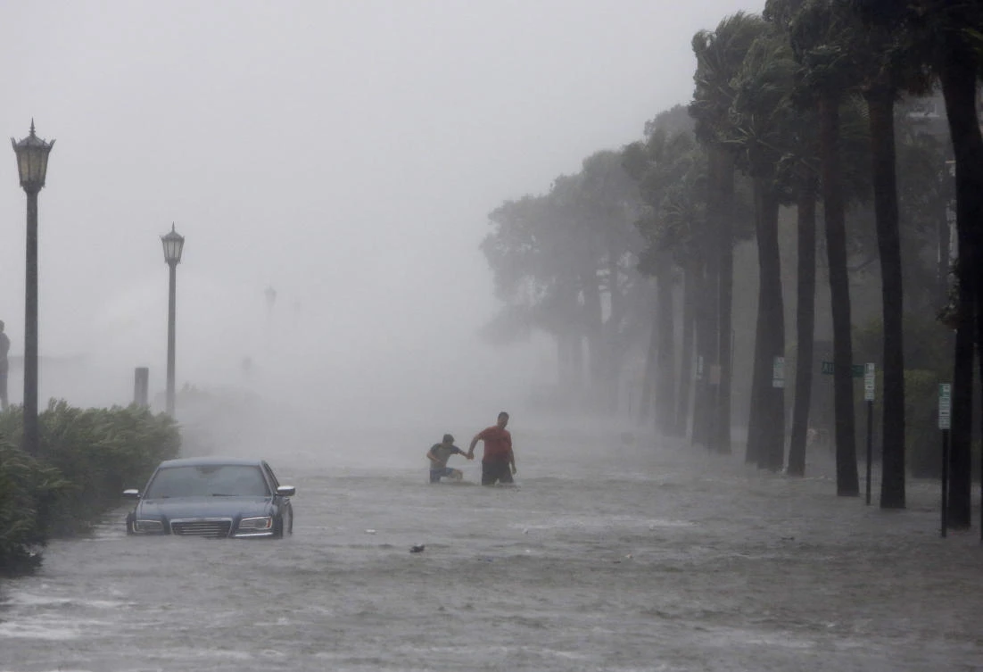 Pedestrians walk by a flooded car on a street as Tropical Storm Irma hits Charleston, S.C., Monday, Sept. 11, 2017. (AP Photo/Mic Smith)w