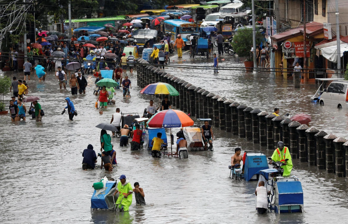 Residents wade and ride on pedicabs along a partially flooded road, in Las Pinas Metro Manila as a storm sweeps across the main Luzon island, Philippines, on September 12, 2017. (REUTERS)