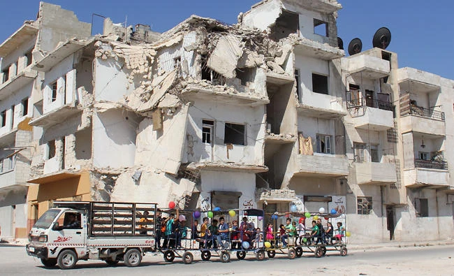 Syrian children ride in carriages decorated in balloons along a damaged street in the northwestern Syrian city of Idlib on September 1, 2017. (AFP)