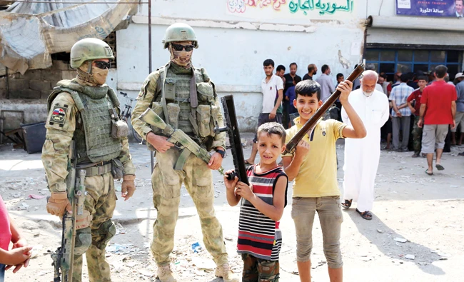 Russian soldiers stand guard in a street in Syria’s eastern city of Deir Ezzor, as local children pose nearby. (AFP)