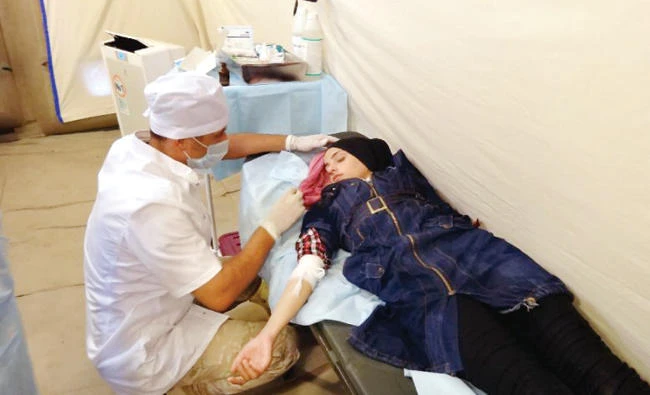 A Syrian woman is attended to by a Russian medical worker at a pop-up facility outside Dar Al-Kabirah, in a humanitarian corridor of a de-escalation zone in central Syria's Homs province. (AFP)