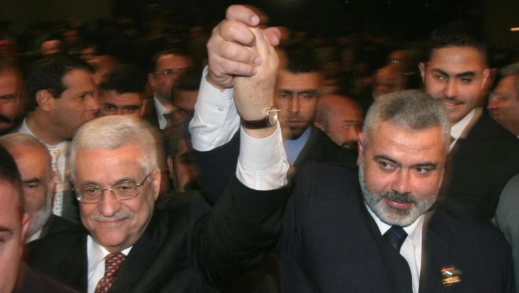 Palestinian Authority President Mahmoud Abbas, left, and Prime Minister Ismail Haniyeh from Hamas, right, raise their linked arms as they move through the crowd at a special session of parliament in Gaza City, March 17, 2007. (File photo by AP)