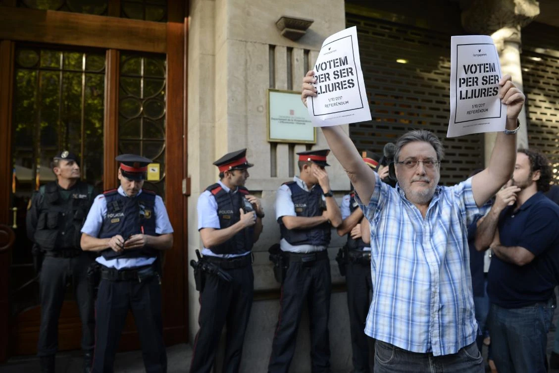 A man holds pro-referendum posters as Spanish Civil Guards and Catalan regional police officers stand in front of the economy headquarters of Catalonia’s regional government in Barcelona on Wednesday. (AFP)