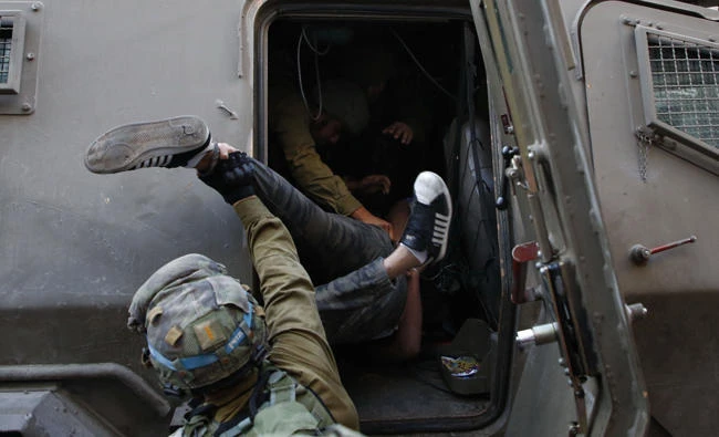 Israeli soldiers force a Palestinian man into an army vehicle after troops entered an area controlled by the Palestinian authority in the divided city of Hebron, in the Israeli-occupied West Bank, on September 20, 2017. Palestinian human rights lawyers on Wednesday handed a 700-page dossier to the International Criminal Court alleging that Israeli authorities are responsible for crimes including apartheid and persecution in the occupied West Bank and East Jerusalem. (AFP / HAZEM BADER)