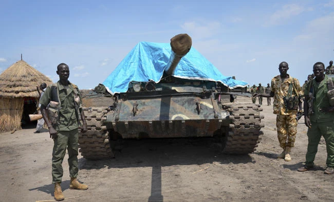 In this photo taken Aug. 19, 2017, government soldiers stand next to a tank they claim captured from the rebels during the latest clashes in June in the town of Kuek, in northern Upper Nile state, South Sudan. South Sudan’s hellish war will get worse if its neighbors let President Salva Kiir hold an election before he accepts peacekeepers, a cease-fire and political opposition, UN investigators said on Wednesday. (AP Photo/Sam Mednick)