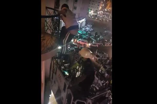 The man climbs down off the balcony as crowds watch below (YouTube)