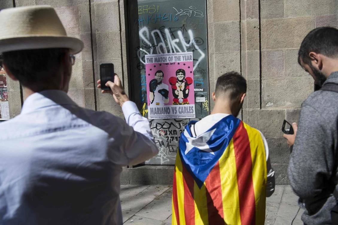 Above, people take pictures of a poster showing Spanish Prime Minister Mariano Rajoy,left, and President of the Catalan Government Carles Puigdemont in Barcelona. (AFP)
