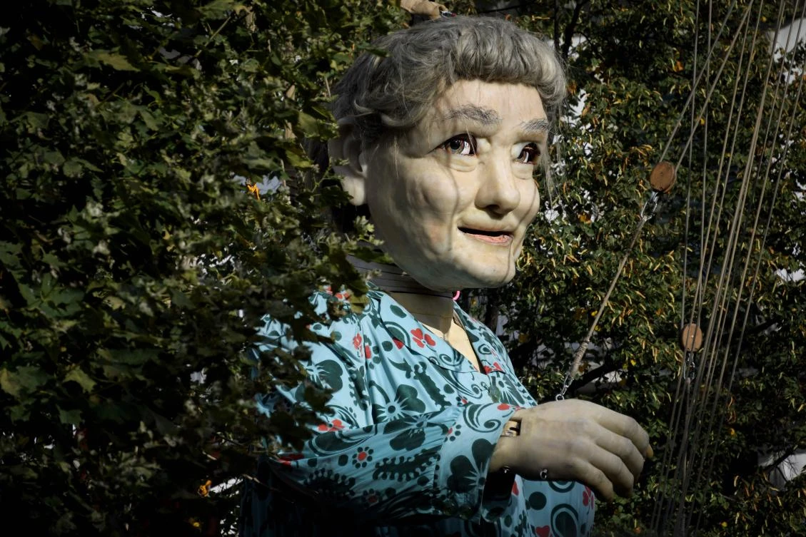 A 7,30 meters high giant animated puppet representing a grandmother created by French street theatre company Royal de Luxe, is seen through foliage during the last act of "The Saga of the Giants" a three days street performance gathering hundred thousand spectators, on October 1, 2017, in Geneva. - / AFP / Fabrice COFFRINI