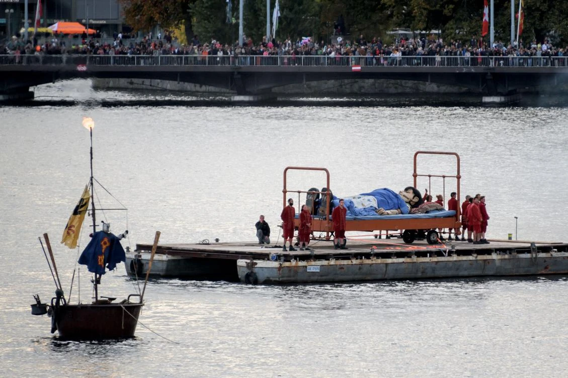 A 5,5 meters high giant animated puppet representing a little girl, by French street theatre company Royal de Luxe, is seen on a bed on Geneva Lake during last act of 'The Saga of the Giants' a three days street performance gathering hundred thousand spectators, on October 1 2017 in Geneva. - / AFP / Fabrice COFFRINI