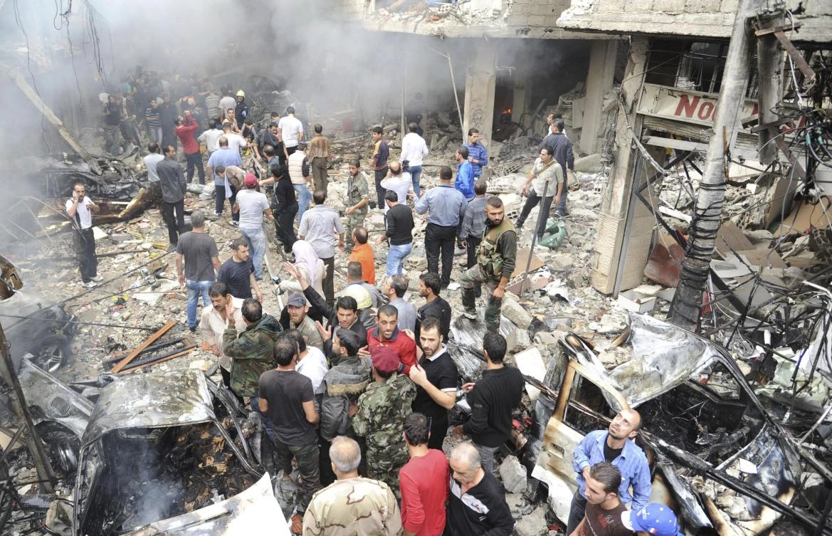 A crowd gathers in front of a building and car damaged after a bomb explosion in the Mezzeh 86 area in Damascus on Monday, November 5, 2012. (File photo: SANA via REUTERS)