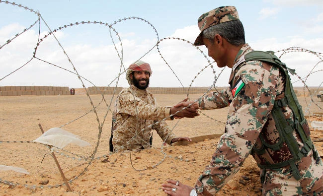 In this Feb. 14, 2017 photo, a member of the Syrian Tribes Army, left, that guards the Syrian side of the berm on the north eastern border with Jordan, shakes hands with a Jordanian soldier. (AP)