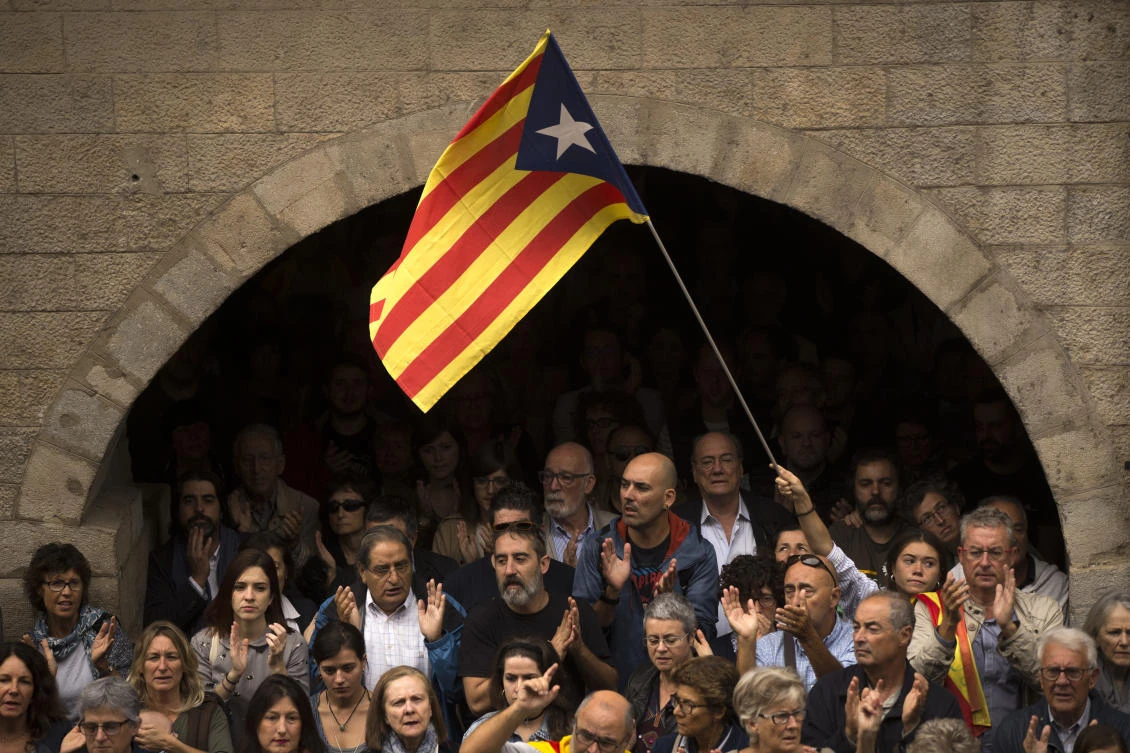 Catalan independence supporters, one waving an "estelada", or Catalonia independence flag, applaud during a rally outside the city hall of Girona, Spain, Monday, Oct. 2, 2017. Spanish riot police smashed their way into polling stations to try to halt a disputed independence referendum in Catalonia on Sunday and fired rubber bullets at protesters outside a Barcelona polling station, with Catalan officials saying more than 330 people were injured, some seriously. (AP Photo/Francisco Seco)