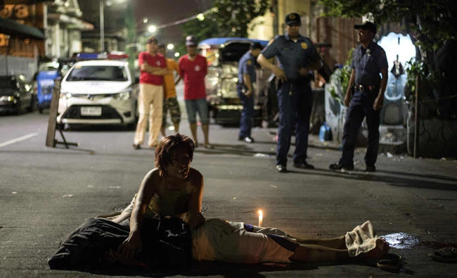 Policemen (back) look at a mother, Nanette Castillo, as she grieves beside the dead body of her son Aldrin, an alleged drug user killed by unidentified assailants in Manila on October 3, 2017. Philippines police officers who want to speak out about "extrajudicial killings and summary executions" in President Rodrigo Duterte's drug war have been offered sanctuary and legal help by the Catholic Church. (AFP / NOEL CELIS)
