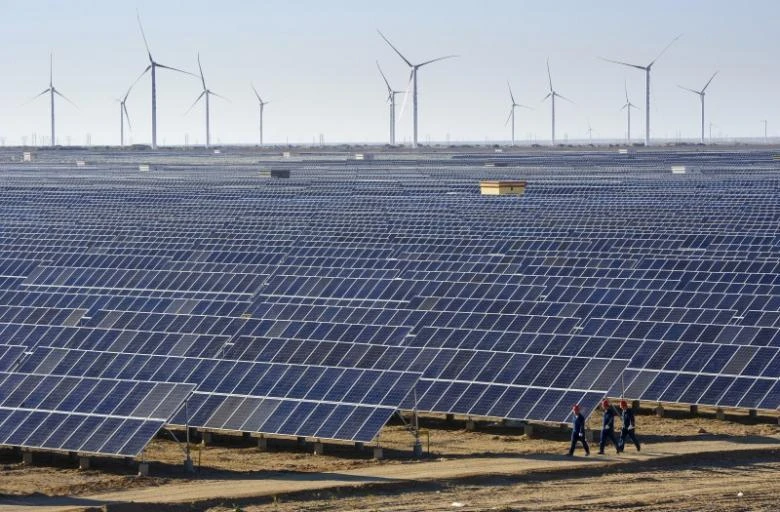 Workers walk past solar panels and wind turbines at a newly-built power plant in Hami, Xinjiang Uighur Autonomous Region, China. (Reuters)