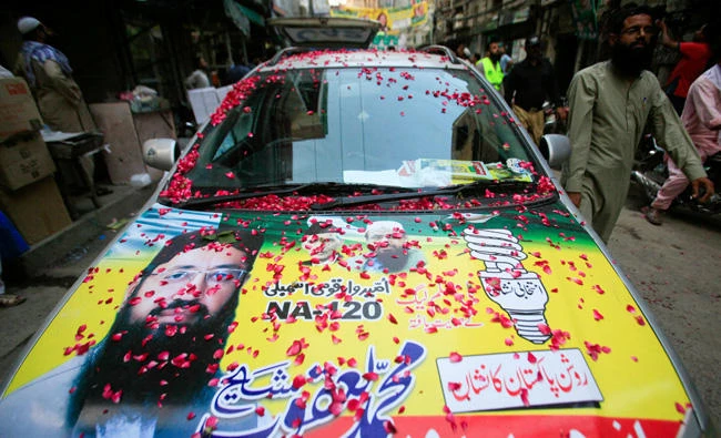 A resident walks past a parked car, decorated with a poster of Mohammad Yaqoob Sheikh, nominated candidate of political party, Milli Muslim League (MML), during an election campaign for the National Assembly NA-120 constituency in Lahore, Pakistan on September 9, 2017. (REUTERS/Mohsin Raza/File Photo)