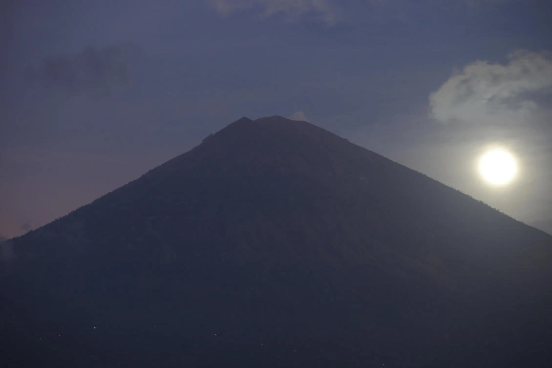 A full moon is set behind the Mount Agung volcano in Karangasem, Bali, Indonesia, on Friday, Oct. 6, 2017. More than 140,000 people have fled from the surrounds of Mount Agung since authorities raised the volcano's alert status to the highest level on Sept. 22 after a sudden increase in tremors. It last erupted in 1963, killing more than 1,000 people. (AP Photo/Firdia Lisnawati)