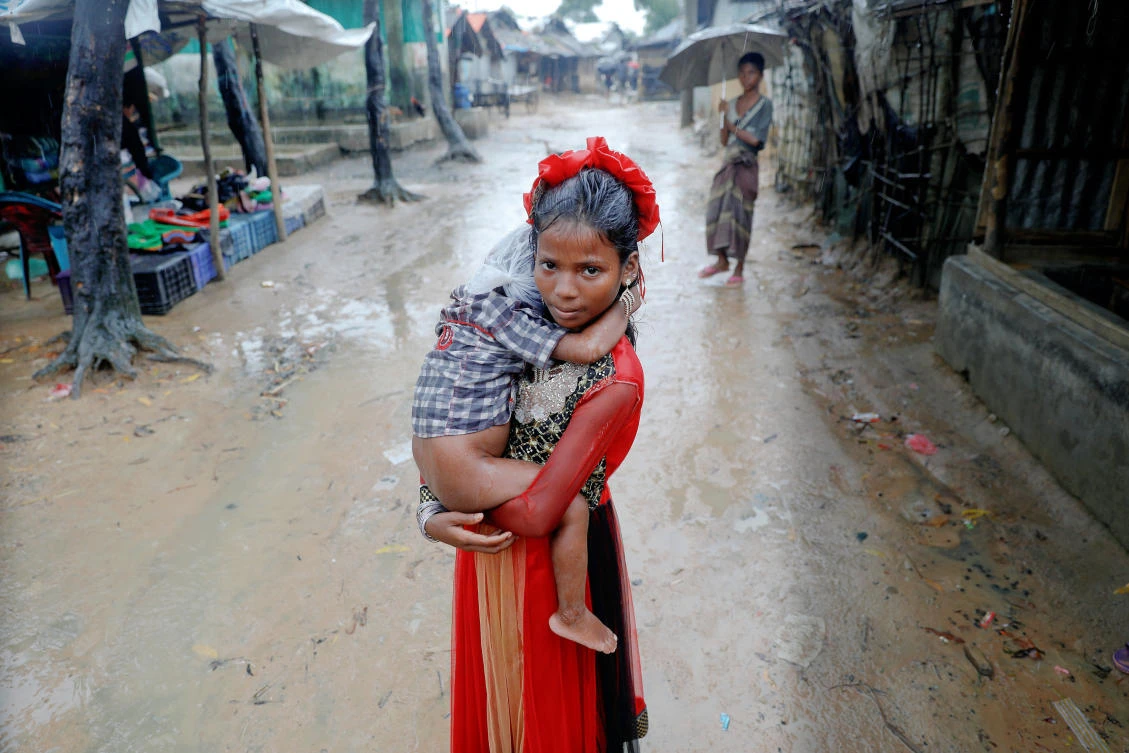 A Rohingya girl, drenched by rain, carries a child through a refugee camp near Cox’s Bazar, on Sunday. (Reuters)