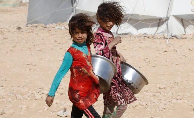 Girls carry containers for food rations on Tuesday at a refugee camp in Ain Issa, Syria. (Reuters)