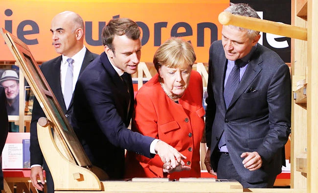 German Chancellor Angela Merkel and French President Emmanuel Macron look on at the printing the declaration of Human Rights on a replica of the Gutenberg press at the Frankfurt Book Fair on Tuesday in Frankfurt am Main, western Germany. (AFP)